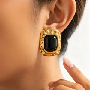 Gros plan de boucles d'oreilles géométriques dorées massives vintage avec pierre noire.