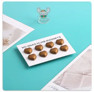 Detaillierte Nahaufnahme goldener herzförmiger magnetischer Hijab-Clips auf weißer Karte.