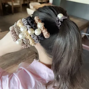 Detail shot of satin hair scrunchies with large pearl decoration, elegant ponytail and bun accessory.
