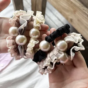 Close-up details of ruffled fabric hair scrunchies with large pearls for elegant styling.