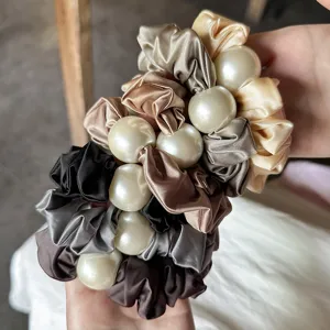 Close-up detail of elegant satin scrunchies with large pearls, premium hair accessories for styling.