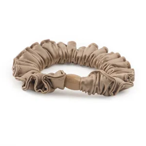 Λεπτομερής εικόνα του πολυτελούς scrunchie από σατέν μετάξι σαμπάνιας με πιέτες.