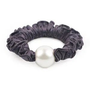 Gros plan de detail du chouchou en satin violet avec une grande perle blanche elegante.