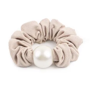 Detail shot of the crinkled beige honeycomb fabric scrunchie featuring a large central white pearl.