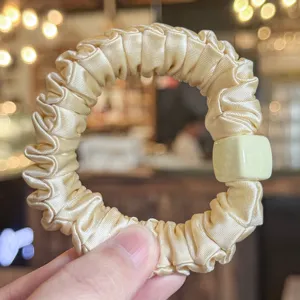 Gros plan détaillé d'un chouchou en satin jaune clair avec un élégant détail de perle carrée.