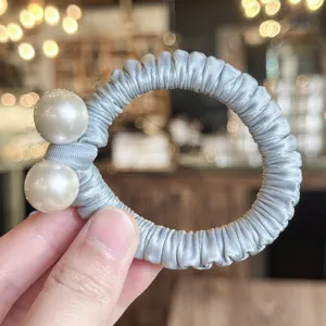 Gros plan sur l'élastique à cheveux double perle, détail chic en satin élastique.