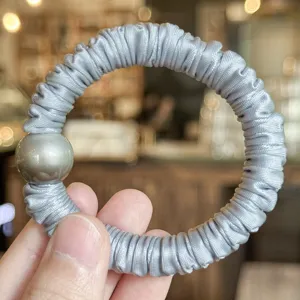 Gros plan détaillé d'un chouchou en satin gris chic doté d'un élégant accent de perle.