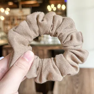 Primer plano detallado de un coletero para el pelo beige texturizado con tela plisada elástica.