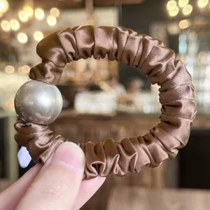 Close-up detail of the brown satin scrunchie featuring a glossy pearl ball decoration.