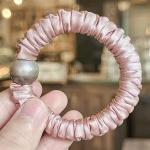 Vue détaillée d'un charmant chouchou en satin rose avec une belle perle grise.