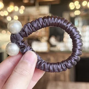 Gros plan détaillé de l'élégant chouchou en satin orné de deux belles fausses perles.