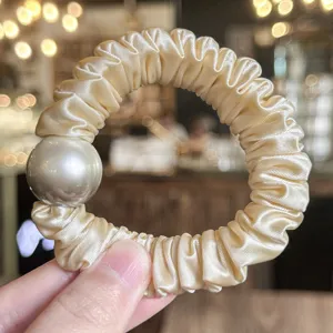 Close-up detail of champagne satin hair scrunchie featuring a large elegant faux pearl accent.