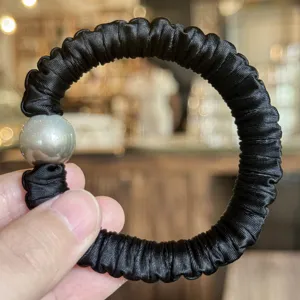 Vue de détail d'un chouchou en satin noir avec perle pour coiffure élégante de femme.