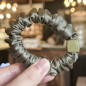 Vue détaillée d'un chouchou en satin vert foncé avec détail carré chic. Souple et élastique.