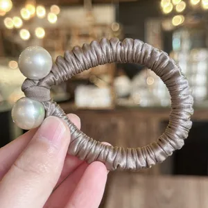 Vue détaillée de l'élastique à cheveux élégant en satin champagne avec deux perles.