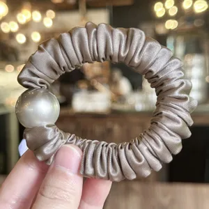 Detailed shot of a chic satin pearl hair scrunchie, elegant elastic hair rope item.