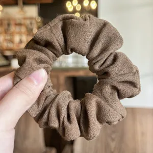 Primer plano detallado de una goma de pelo marrón con textura de lino y gran elasticidad.