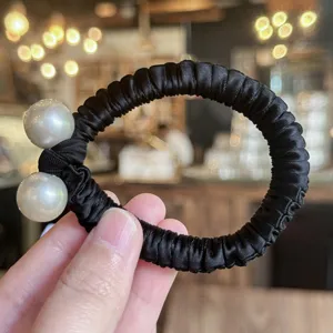 Gros plan détaillé de l'élastique à cheveux noir en satin avec deux grandes perles.