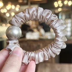 Detail shot of an elegant satin hair scrunchie with a large metallic bead for women.