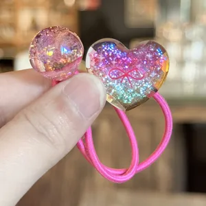 Gros plan détaillé de liens pour cheveux en résine scintillante avec cœur et boule rose doux.