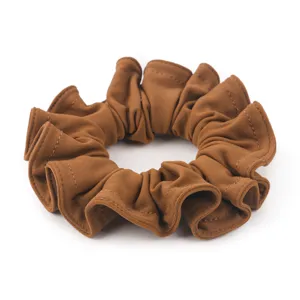 Dettaglio scrunchie in camoscio marrone, elegante accessorio per capelli con fascia elastica.
