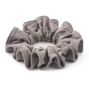 Primo piano dettagliato di scrunchie in morbida finta camoscio, design plissettato taupe elegante.
