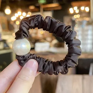 Closeup view of dark brown satin hair scrunchie with large white pearl detail accessory.