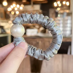 Close-up detail of grey satin hair scrunchie with large white pearl accent for styling.
