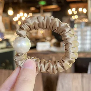 Detail shot of elegant champagne satin hair scrunchie adorned with a large faux pearl.