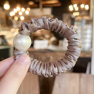 Close-up detail of an elegant satin hair scrunchie featuring a large faux pearl decoration.