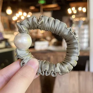 Detailed shot of a luxury satin scrunchie featuring an elegant large pearl charm in soft green.