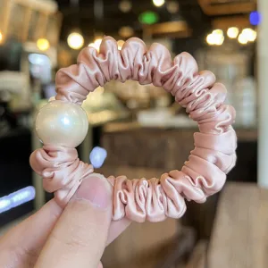 Detailed shot of pink satin hair scrunchie featuring a large elegant pearl decoration.