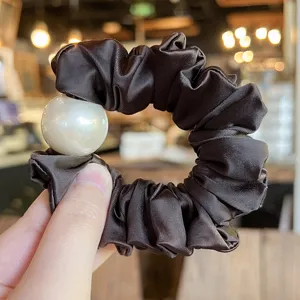Dark brown satin hair scrunchie detail view with elegant large white pearl decoration accessory.