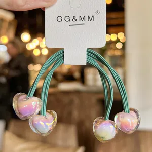 Élastiques à cheveux verts avec pendentifs cœur irisés lumineux sur carte de présentation.