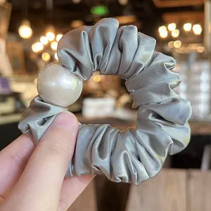 Close-up detail of grey satin hair scrunchie adorned with a large elegant faux pearl decoration.