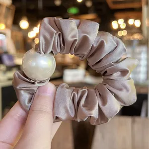 Detail view of satin hair scrunchie with large pearl decoration, elegant and stylish hair tie.