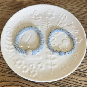 Close-up of light blue pleated hair scrunchies with decorative beads on white plate.