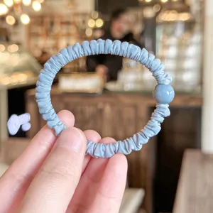 Close-up of light blue pleated hair tie with cute round bead, soft elastic daily hair accessory.
