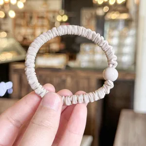 Close-up detail shot of a beige pleated hair scrunchie with a round bead, soft and elegant style.