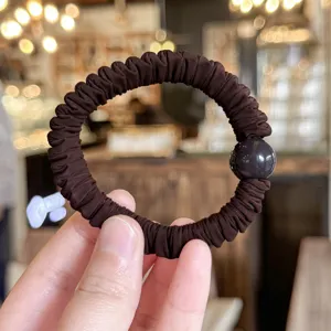 Detailed shot of dark brown pleated hair scrunchie with smooth round bead accessory.