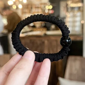 Detail shot of a black pleated hair scrunchie with a glossy black bead, high elastic design.