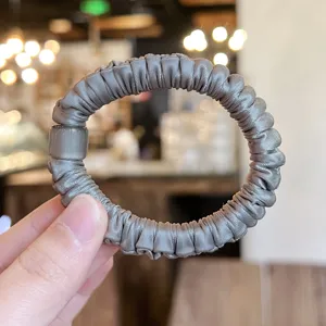 Minimalistischer grauer Satin-Haargummi mit Katzenaugen-Perle für elegante Alltagsfrisuren.