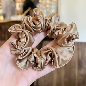 Gedetailleerd aanzicht van een luxe gouden satijnen haarscrunchie met gladde textuur.