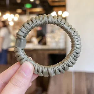 Nahaufnahme Detail des grauen Satin Haargummis mit süßem Perlenakzent für tägliches Haarstyling.