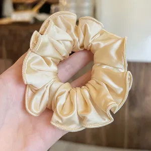 Gedetailleerde close-up van een stijlvol beige satijnen haarelastiekje met een zachte glans.
