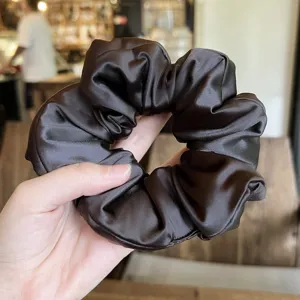Dark brown satin scrunchie detail view, soft stuffed hair accessory closeup photography.