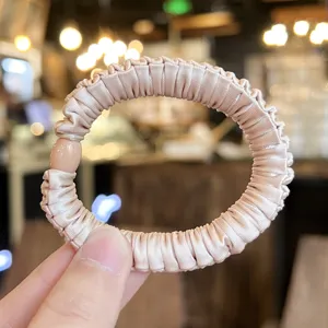 Close-up detail of champagne satin scrunchie hair tie with high elasticity and bead decor.