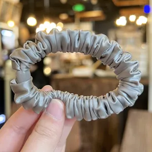 Detail shot of a grey satin scrunchie, soft hair tie showing smooth fabric texture close up.