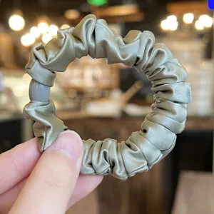 Close-up detail shot of the elegant satin hair scrunchie featuring a smooth decorative bead.