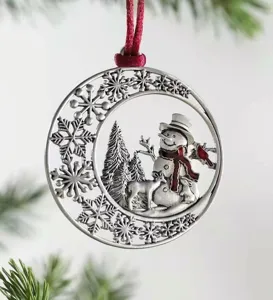 Close-up of vintage metal Christmas tree ornament featuring a carved snowman and deer design.